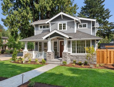 Beautiful luxury home exterior on bright sunny day with green grass and blue sky. Features walkway, covered porch, and stately gables and columns.