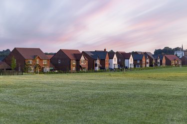 Grass area by residential houses under clouds at sunset