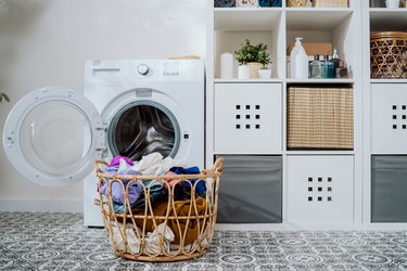 Closeup of clothes in basket, open washing machine standing in background, weekend cleaning, household chores, laundry room.