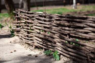 A woven wooden fence made of thin old branches in the countryside. Village yard fence from wood. Shallow depth of field.