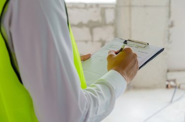 foreman builder, engineer or inspector in green safety vest reflective checking and inspecting with clipboard at construction site building interior, inspection, contractor and engineering concept