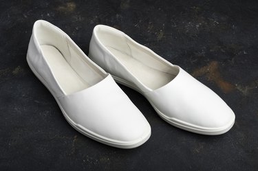 White leather slip-on shoes on black background.