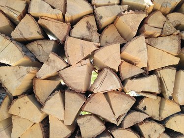 Chipped firewood is on the heap. Woodpile of firewood close-up. A stack of dry firewood, visible texture and cracks in the tree. Exterior shot of a large pile of firewood in soft daylight