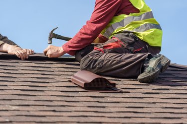 Two skilled roofers installing asphalt shingles or roof tile on top of new house.