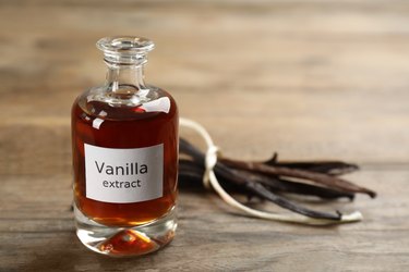 Aromatic vanilla extract and dry pods on wooden table, space for text