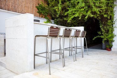 Four empty bar stool chairs with wooden seats and metal foot near a white concrete bar counter.