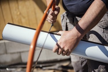 Roofer cutting roof gutter with  hand saw