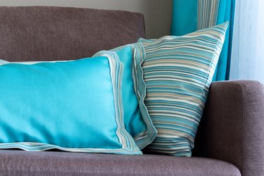 Bright blue designer pillows on a plain brown sofa by the window, interior details closeup