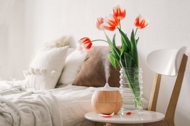 Aroma oil diffuser on chair with cut tulips in bedroom.