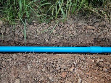 Small PVC pipe lying in a trench near pavement for water supply system.