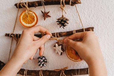 Decorating handmade craft Christmas tree made from sticks and other natural materials hanging on wall. Sustainable Christmas, zero waste, plastic free, eco friendly.