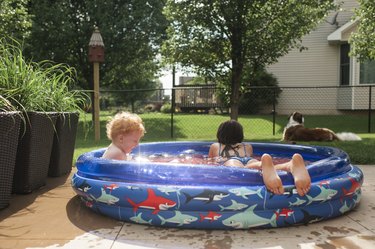 Siblings playing in backyard wading pool.