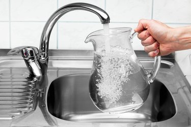 Pitcher being filled with drinking water from kitchen faucet.