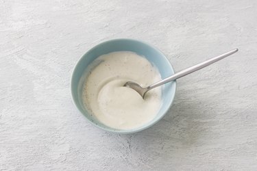 Blue bowl with salad dressing from sour cream, mayonnaise, wine vinegar and spices on a light gray background