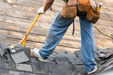 Roofer removing old shingles from roof of house