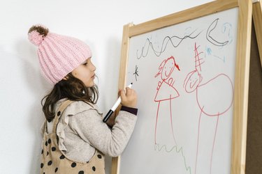 Girl with knit hat drawing on whiteboard at home.