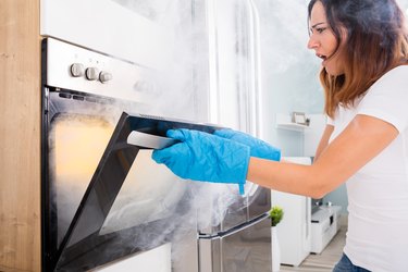 Woman Opening Door Of Oven Full Of Smoke