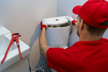 plumbing services - plumber working in bathroom installing toilet wc water tank
