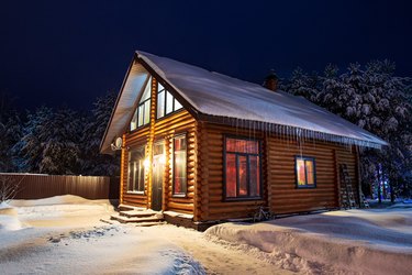 Rustic log house, snow-covered pine trees, snowdrifts, fabulous winter night.