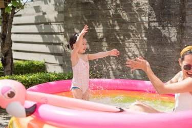 A toddler splashes water on her mother while playing in an inflatable pink pool.
