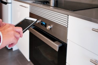 a woman using a smartphone to control the oven in the kitchen - intelligent home concept