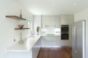 White kitchen with heat or smoke detector on ceiling, vase of flowers on counter, built-in stainless double ovens.