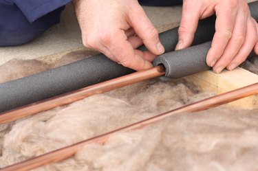 Close-up of man installing insulation on copper water pipe