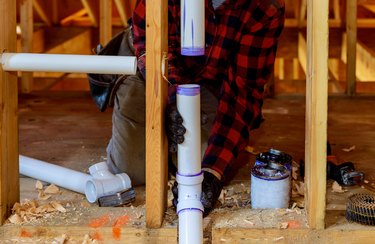Plumber installing primer and glue PVC pipe at construction home