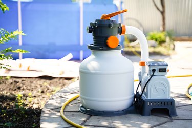 Sand filter system for purifying pool water on the background of a frame polyethylene pool.