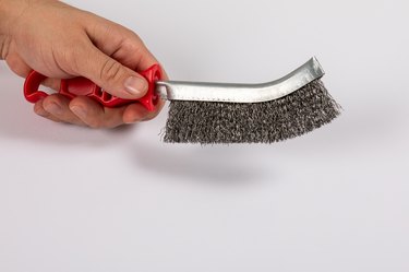 Metal wire brush with red plastic handle in a man's hand. White background