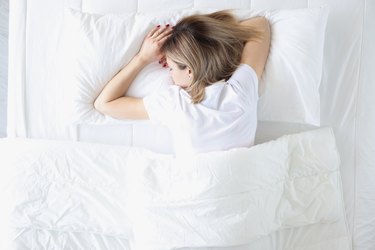 Young woman sleeping on her stomach in white bed top view