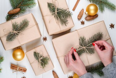 Christmas gift wrapping background, copy space. Female hands holding christmas present box wrapped in kraft, top view. Winter holidays concept, flat lay. Woman with red manicure packing Christmas gift