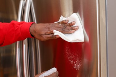 Cleaning a stainless steel French door refrigerator in a kitchen.