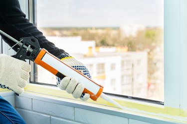 Contractor hand holding glue gun with silicone to repair tile and window. Installation or renovation interior concept.