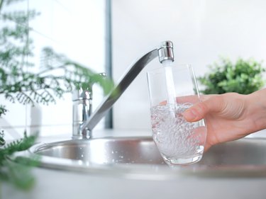 A stream of clean water drink flows into the glass. Woman holding a glass of water under running water from the tap in the kitchen