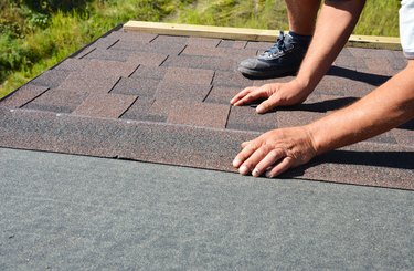 A building contractor is installing dimensional asphalt roof shingles on the underlayment of the house construction repairing the rooftop.