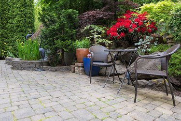 Garden backyard with lush plants landscaping pond water fountain and stone paver patio hardscape with wicker bistro furniture chair and table set