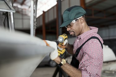 Boat owner uses a hand power drill to fix a boat while working in a boathouse. Boat Repairing, Fiberglass Craft Hobby Concepts.