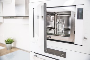 Built-in microwave oven with door ajar, white kitchen.