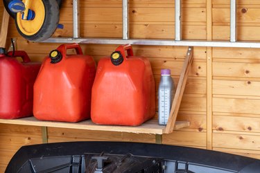 Garage corner with three red plastic fuel cans , staircase and snow plough for atv with wooden wall on background. Petrol gas containers reserves storage at vehicle home garage
