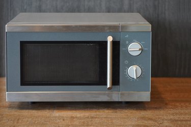 front view old grey and silver microwave oven on wooden floor background, decor, technology, fashion, copy space