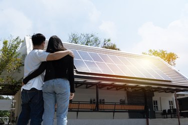Happy couple standing near their house with solar panels.