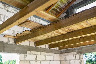 Wooden joists prepared for laying the attic floor of a newly built white brick house.