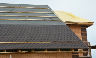 How to install asphalt roof shingles: A close-up of asphalt shingles installation on the roof covered with water-resistant underlayment without  fascia board and a roof sheathed with plywood.