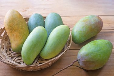 Mangos in woven tray on wooden table.