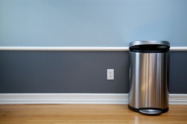 Empty wall with modern trash can and electical outlet.