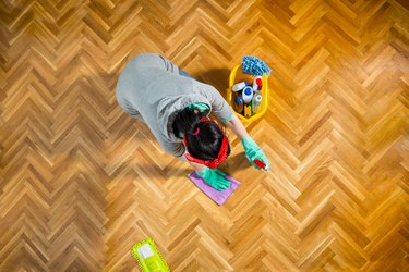 Woman cleaning parquet floor while kneeling at home.