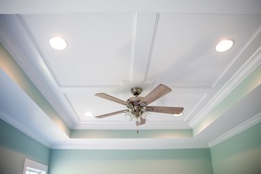 White tray ceiling in small new construction house with windows and a fan