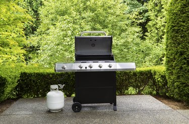 Large outdoor bbq cooker with white propane tank on home concrete patio