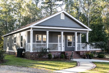 Close up of small blue gray mobile home with a front and side porch with white railing.